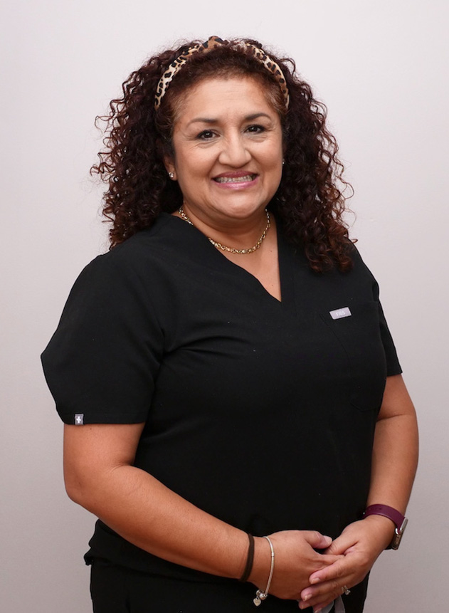The image is of a woman in a professional attire, likely a nurse or healthcare worker, posing for a portrait with a friendly expression.