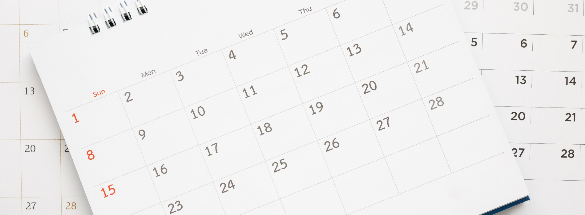 The image displays a calendar with the month of April 2023 visible, placed on top of another calendar that is partially obscured. Both calendars have a printed grid format and are set against a blurred background.