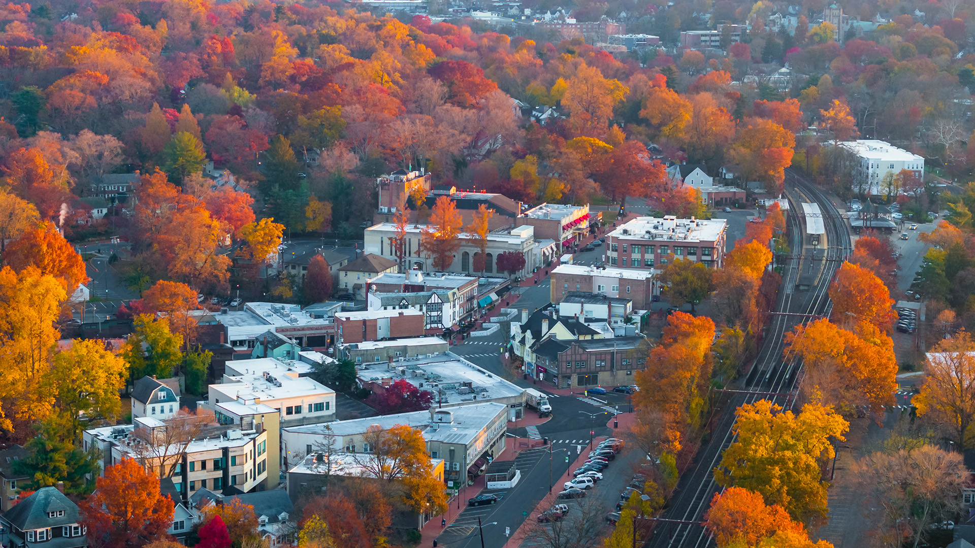 Autumnal scene of a residential neighborhood with vibrant red and orange leaves on trees, set against the backdrop of a clear sky.