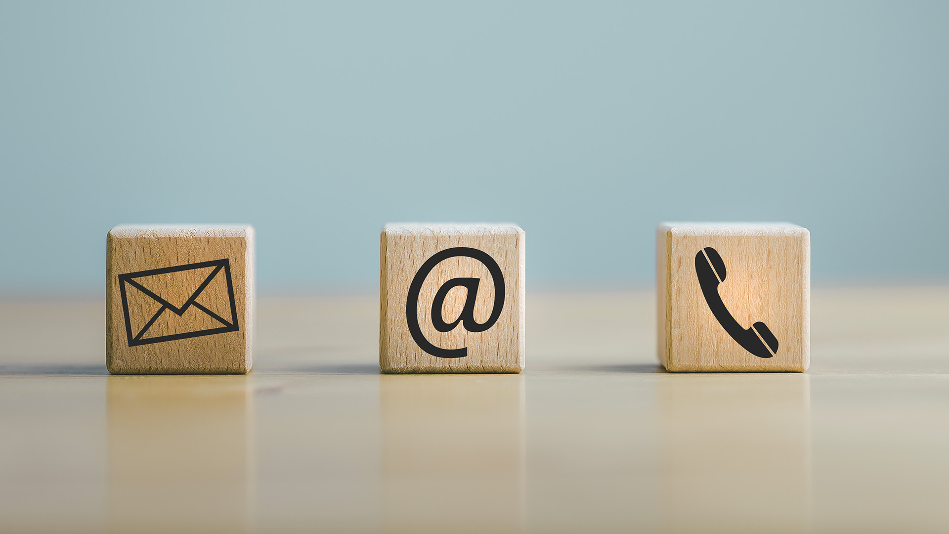 Three wooden blocks with email, phone, and chat icons, symbolizing communication methods.