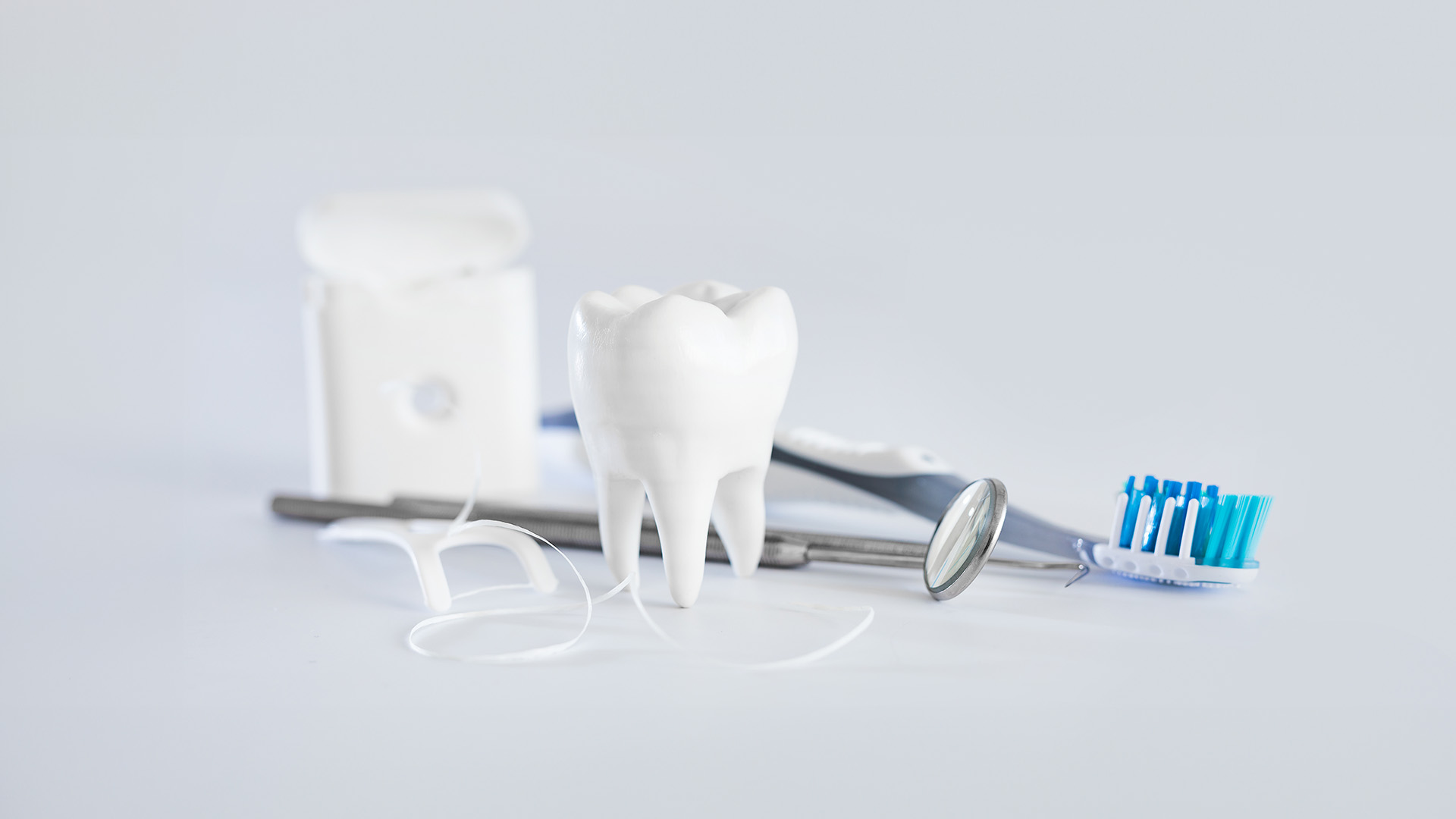 The image shows a toothbrush and dental floss placed next to each other, with an object that resembles a dental implant or prosthesis also present.