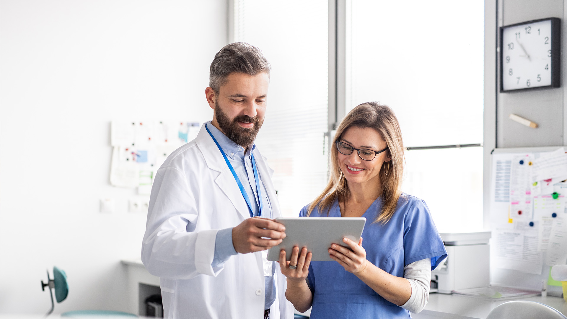 A healthcare professional and a patient in a modern medical setting, with the professional holding a tablet and both looking at it.