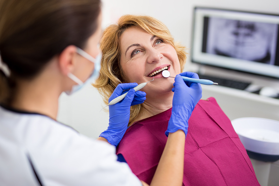 Dentist performing a dental procedure with patient wearing a purple gown and blue gloves.