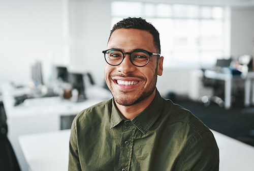 The image is a photograph of a smiling man in an office setting, wearing glasses and a green shirt.