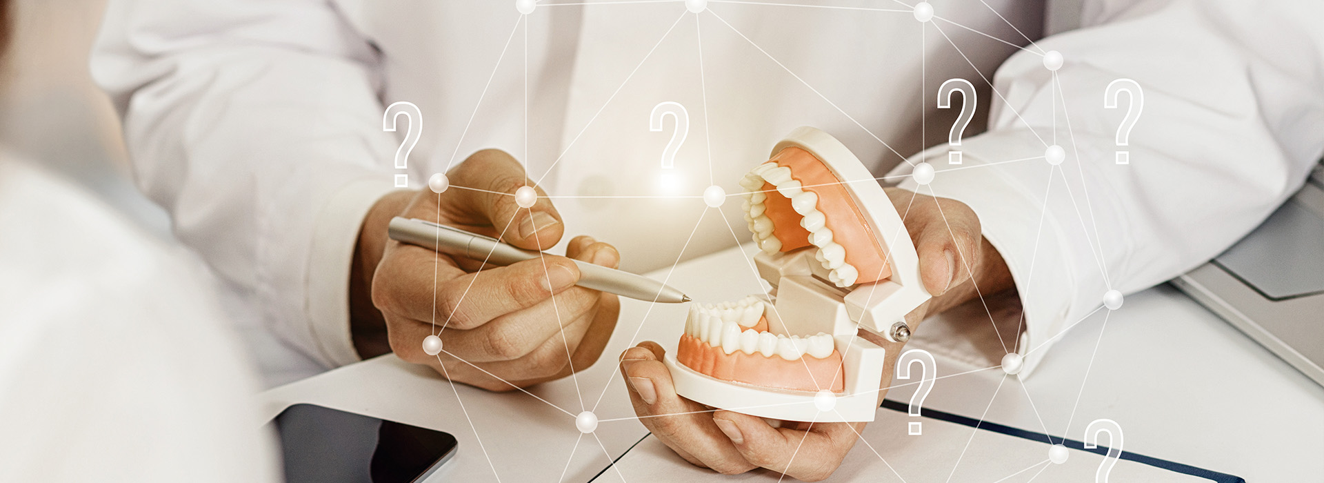 A person s hand holding a dental model with a digital interface showing numerical values and a question mark, suggesting a focus on dental care or technology.