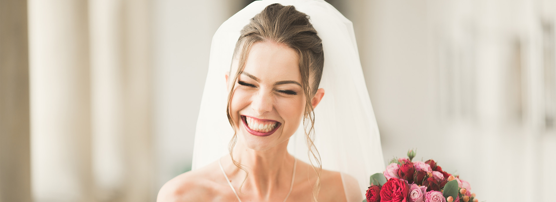 The image is a photograph of a woman wearing a wedding veil and holding a bouquet, smiling and looking away from the camera.