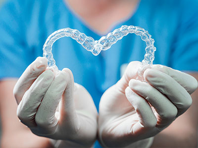 A person s hand holding a transparent heart-shaped dental appliance against a blue background.