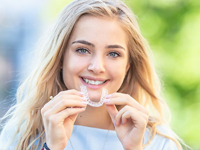 A young woman with a radiant smile holds up a toothbrush, showcasing its design.