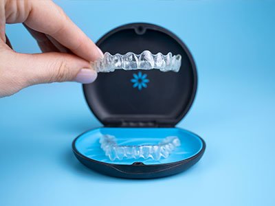Clear plastic dental retainer with blue base, being held up by a hand.