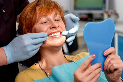 The image shows a woman sitting in a dental chair, receiving dental care, with a dental hygienist assisting her.