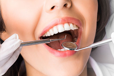 A woman with a wide smile, wearing white gloves and holding dental tools, is seen in the foreground.