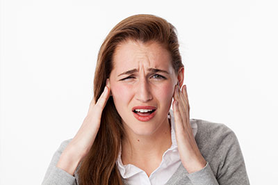 A woman with a pained expression is holding her head with both hands, possibly in discomfort or distress.