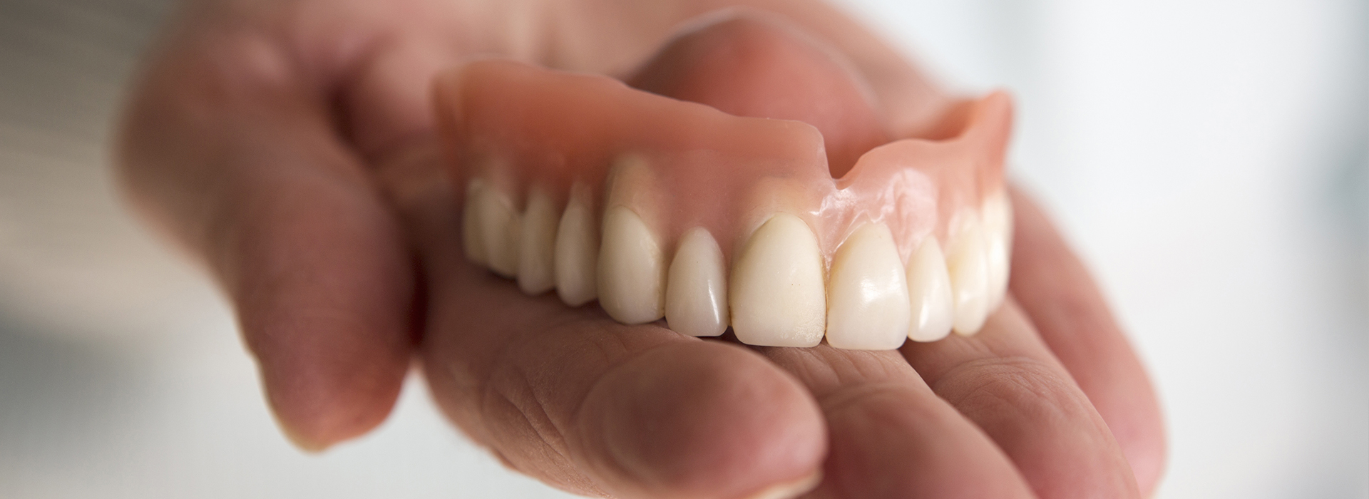 An elderly person s hand holding a set of dentures.