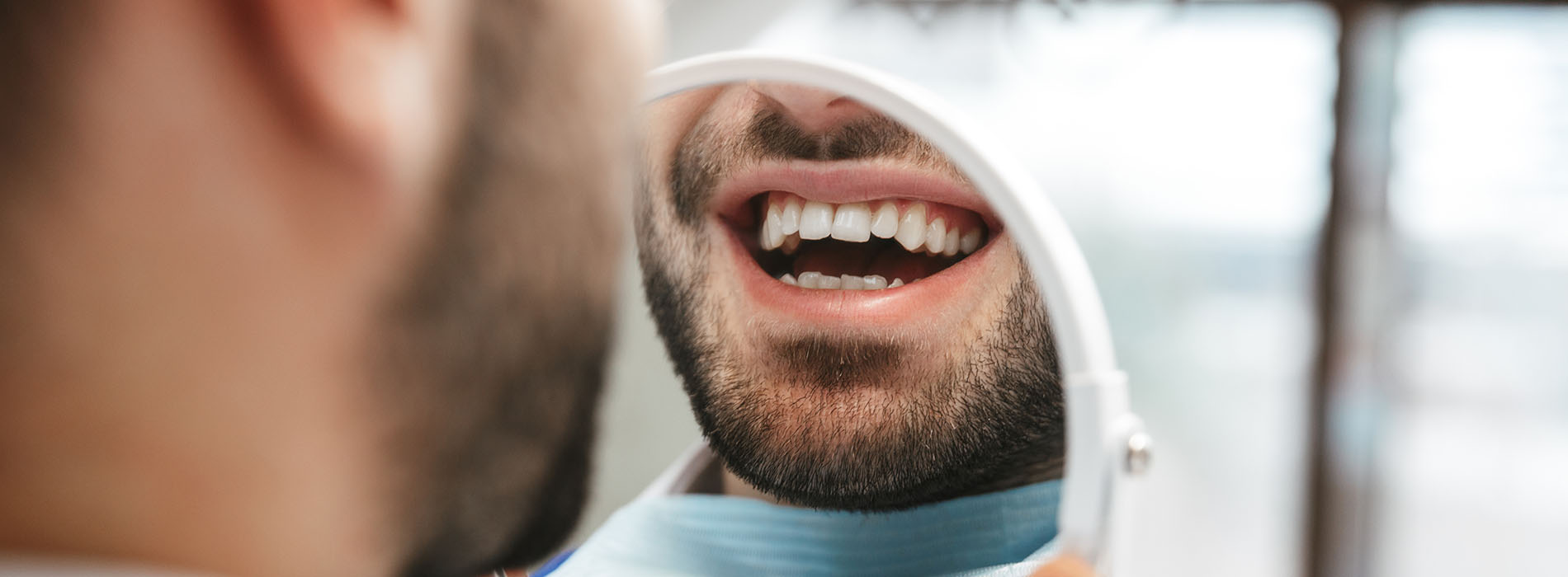 A man with a beard is smiling, and his reflection is visible in a mirror.