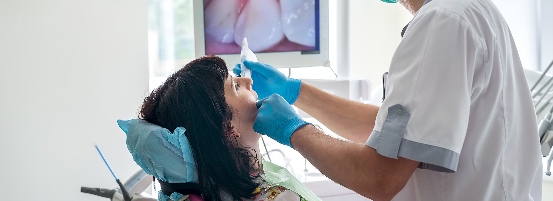 A dental professional performing a procedure on a patient, with medical equipment and a chair visible.