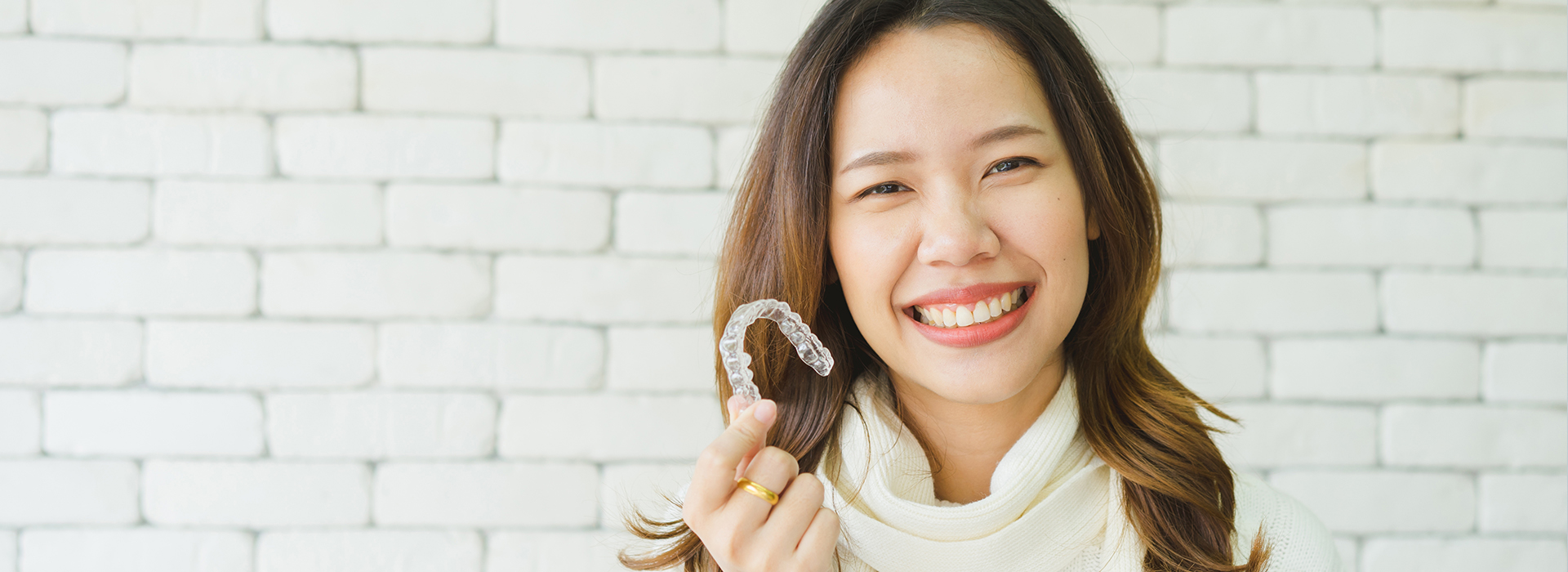 A woman with a radiant smile, holding a ring and standing in front of a brick wall.