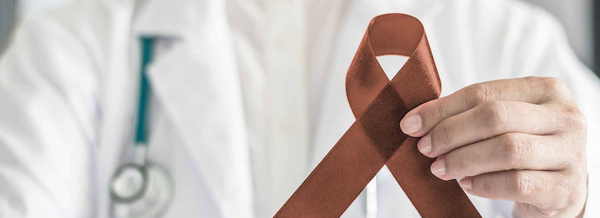 The image features a person in a white lab coat holding up a red ribbon with a brown bow on it, signifying awareness for a specific cause.