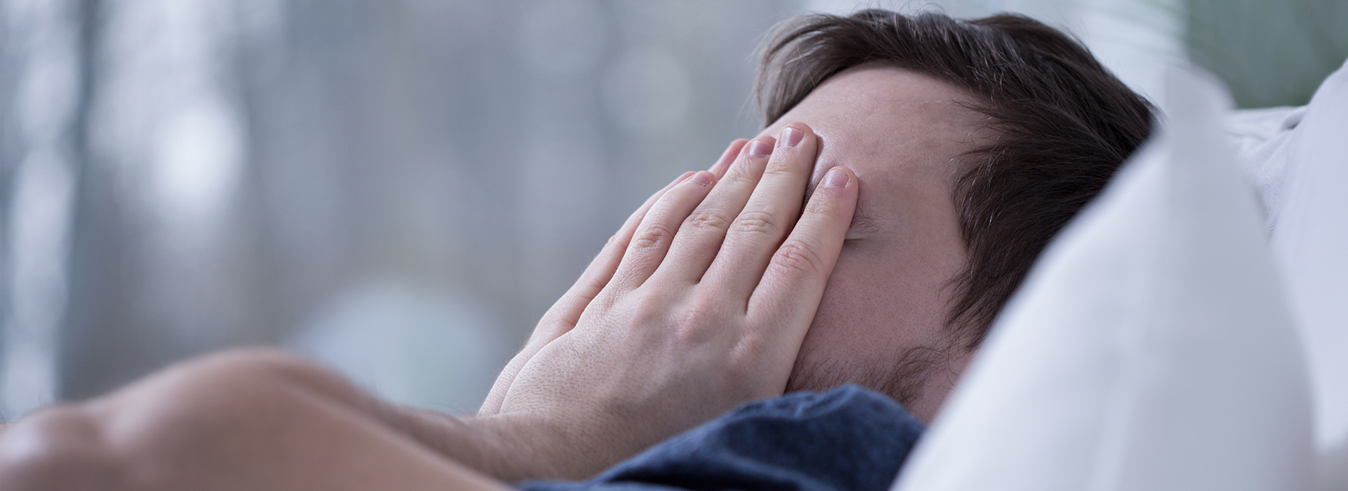 A person lying in bed with their face partially covered, possibly by a hand or arm.