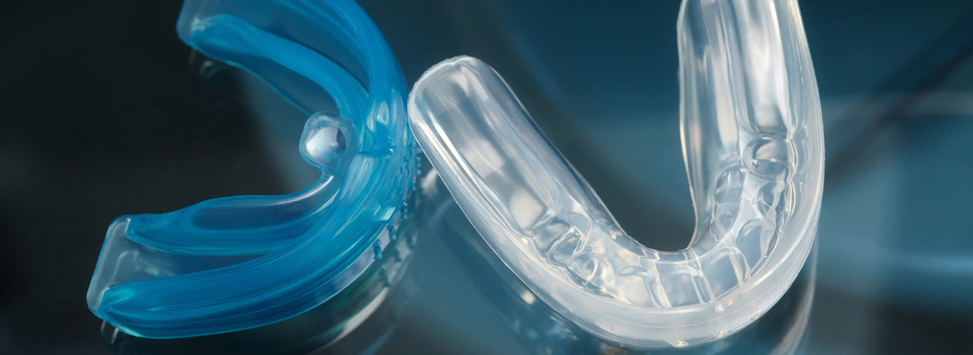 The image shows a close-up of a clear, plastic dental retainer with blue accents and a transparent, circular object in the background.