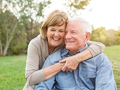 An elderly couple, a man and a woman, are embracing each other in a warm hug.