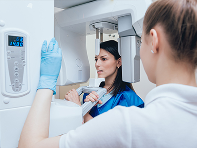 A woman in a blue uniform standing next to a large, modern dental X-ray machine, with another person observing the equipment.