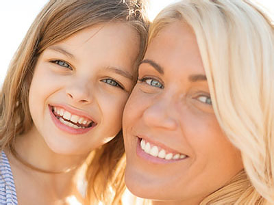 A woman and a young girl are smiling at the camera, with the woman s face partially obscured by the child.