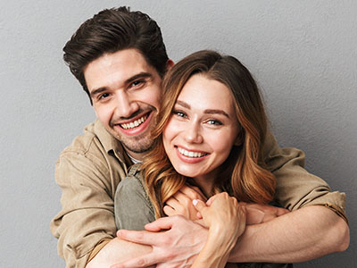 A man and woman in a warm embrace, smiling at the camera.