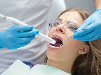 Woman receiving dental treatment with a dentist using a white device to clean her teeth.