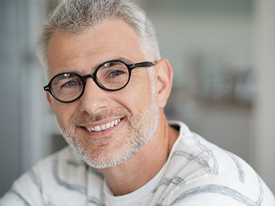 A man with gray hair, glasses, and a beard is smiling at the camera.