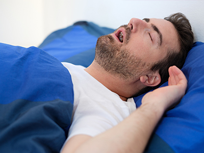 Man lying in bed with eyes closed, appearing to be asleep or resting.