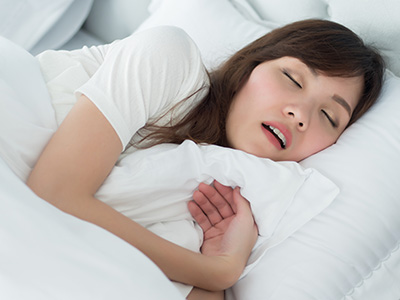 A woman sleeping peacefully on a bed, with her hand placed over her mouth.