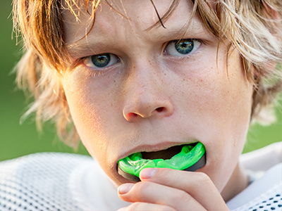 A young boy with blonde hair and a green toothbrush in his mouth, captured in a close-up shot.