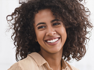 A smiling young woman with curly hair, wearing a beige top, against a white background.